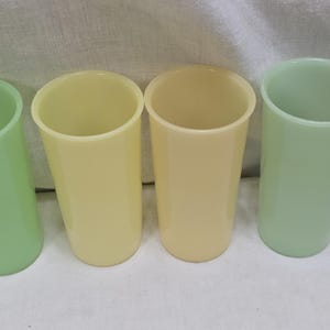 May include: Four vintage drinking glasses in pastel colors. Two are light green, and two are yellow. The glasses are cylindrical with a smooth, glossy finish. They are arranged side by side, showcasing their simple, classic design.