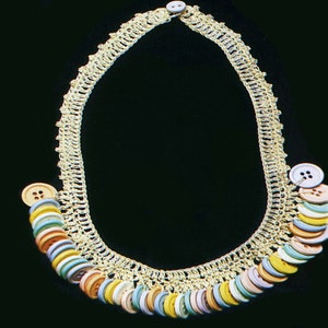 May include: A gold crocheted necklace with a row of colorful buttons. The buttons are in various shades of blue, pink, yellow, and orange.