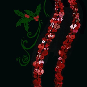 May include: A long necklace made of red and pink buttons, arranged in a swirling pattern. The necklace is on a black background with a green holly leaf design.