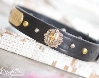 May include: Black leather dog collar with silver and gold accents. The collar features a silver cross charm and a gold nameplate engraved with the word "JOY".