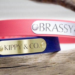 Pode incluir: Duas coleiras para c&atilde;es com etiquetas de nome personalizadas. A coleira superior &eacute; rosa com uma etiqueta prateada que diz "BRASSY". A coleira inferior &eacute; azul marinho com uma etiqueta dourada que diz "KIPPY & CO."