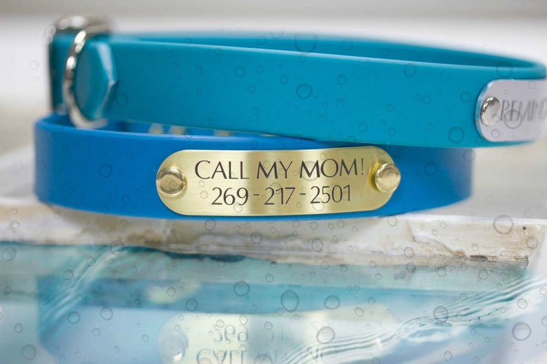 Pode incluir: Duas coleiras de c&atilde;o azuis com etiquetas de nome de metal dourado. A coleira superior &eacute; azul turquesa e a coleira inferior &eacute; azul mais escuro. A etiqueta de nome na coleira inferior diz "CALL MY MOM! 269-217-2501".
