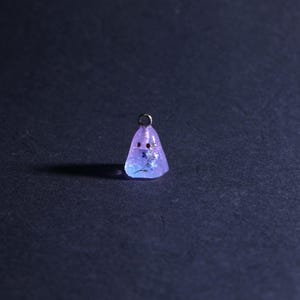 May include: A small, lavender resin ghost pendant with two red dot eyes and a silver loop. Tiny blue flowers are encased within the resin. The pendant is set against a dark backdrop. A unique, handcrafted jewellery item.