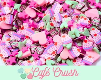 May include: Assortment of pink, green, and white resin charms in the shape of hearts, stars, cupcakes, and coffee cups. The charms are scattered on a light green background with the text "Cafe Crush" in pink.