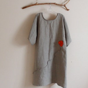 May include: A gray linen dress with a red flower applique on the front. The dress has a scoop neck and short sleeves.