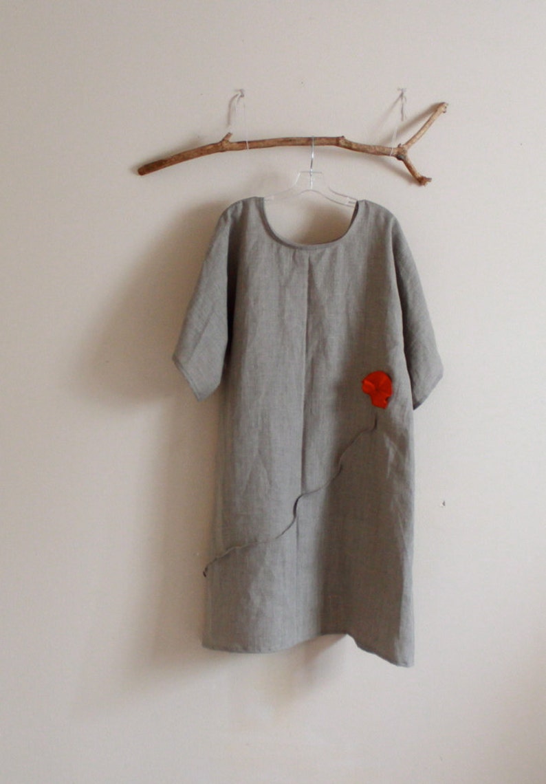 May include: A gray linen dress with a red flower applique on the front. The dress has a scoop neck and short sleeves.