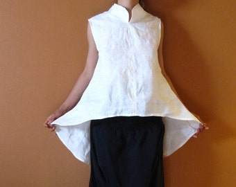 May include: A white linen sleeveless top with a high collar and a slightly asymmetrical hemline. The top is loose-fitting and has a relaxed, casual style.