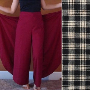 May include: A pair of wide-leg pants in a deep burgundy color with a long, flowing wrap skirt attached. The skirt is made of the same fabric as the pants and has a black and white plaid pattern.