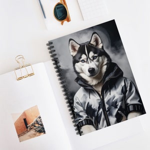 May include: A black and white husky dog wearing a gray and black jacket with a hood. The dog is looking directly at the camera. The background is a gray and white cloudy sky.