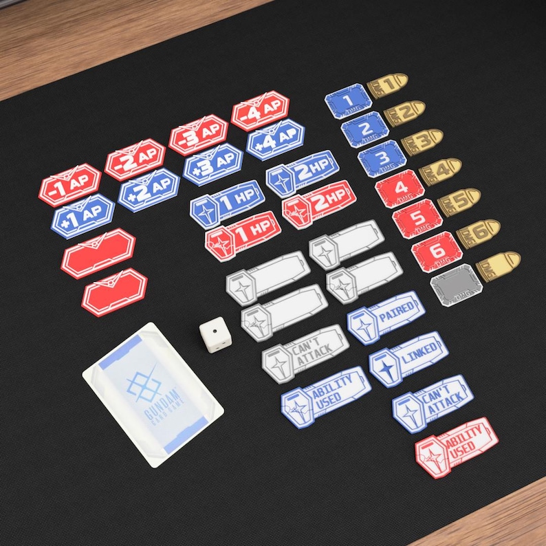 May include: A collection of game components, including tokens, cards, and dice, arranged on a black surface. The tokens feature text like "AP" and "HP", with numbers and phrases such as "Can't Attack" and "Ability Used". A card with the text "GUNDAM" is also present.
