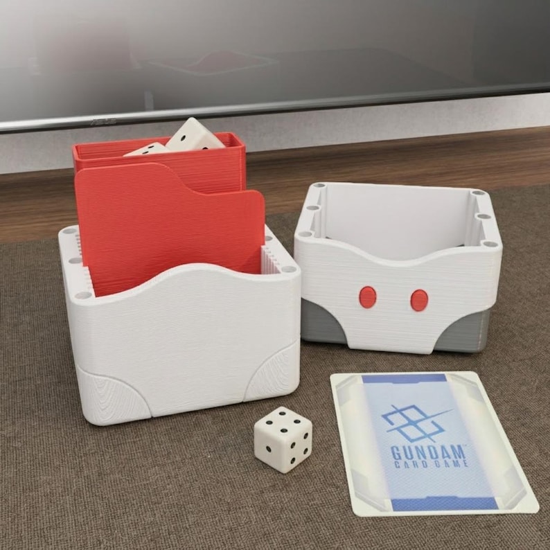 May include: White and red card game storage boxes with a dice and a card. The boxes have a wood grain texture. One box has red dividers. The card has the text "GUNDAM CARD GAME" and a blue and white design.