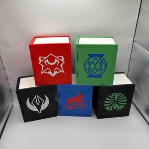 May include: Six colourful, cube-shaped storage boxes. The boxes are red, green, black, blue, and black. Each box has a white interior and a unique graphic design in a contrasting colour on the front. The boxes are arranged in two rows.