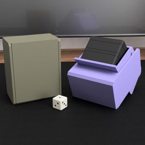 May include: A white die with black dots sits on a black surface next to a light green box and a purple box containing a black object. The boxes appear to be made of wood or a similar material. The scene is set against a neutral background.