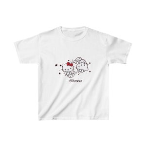 Puede incluir: Camiseta blanca con un gráfico de dos personajes de Hello Kitty vestidos como signos del zodíaco Piscis. El texto "Piscis" está impreso debajo de los personajes.