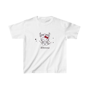 Puede incluir: Camiseta blanca con una imagen de dibujos animados de Hello Kitty vestida como un signo del zodíaco Tauro. La imagen incluye el texto "Taurus".