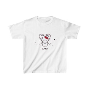 Puede incluir: Camiseta blanca con una imagen de dibujos animados de Hello Kitty vestida como el signo del zodíaco Aries. La imagen está en blanco y negro con acentos rojos. El texto "Aries" está impreso debajo de la imagen.
