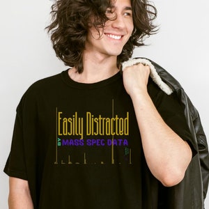 May include: A black t-shirt with the text "Easily Distracted by MASS SPEC DATA" in gold and purple lettering.