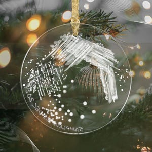 Könnte beinhalten: Ein transparenter Weihnachtsbaumschmuck aus Glas mit einem weißen abstrakten Design und dem Text "SAMPLE 23DEC SOS" auf der Vorderseite.