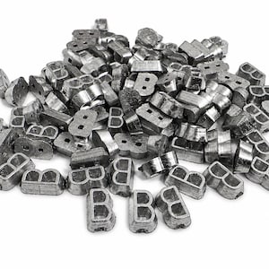 Puede incluir: Un montón de pequeños objetos metálicos con forma de letra "B". Los objetos son de color plateado apagado y parecen ser de metal. Están dispersos sobre un fondo blanco, con algunas letras orientadas verticalmente y otras de lado.
