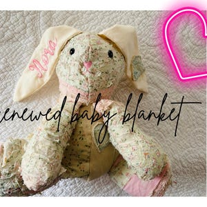 May include: A handmade bunny-shaped baby blanket with floral fabric and pink accents. The bunny's ear is embroidered with the name "Nora" in pink script. The blanket has the words "renewed baby blanket" in a handwritten font.