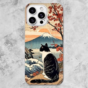 K&ouml;nnte beinhalten: Eine Smartphone-H&uuml;lle mit einem Grafikdruck einer schwarz-wei&szlig;en Katze, die auf einem Felsen sitzt und auf eine Landschaft mit einem gro&szlig;en Berg, einem Gew&auml;sser, brechenden Wellen und einem Baum mit roten Bl&uuml;ten blickt.