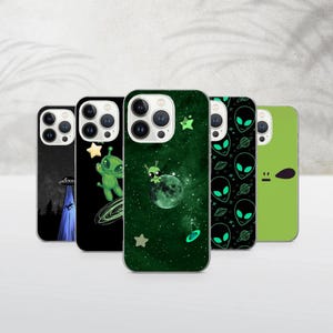 May include: A collection of five phone cases with alien-themed designs. The cases feature various illustrations, including a UFO, an alien with a star, an alien on a moon, a pattern of alien faces, and a solid green case with a simple design.