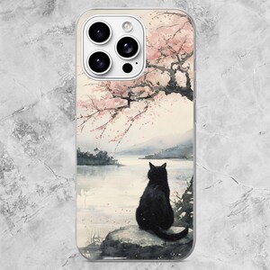 K&ouml;nnte beinhalten: Eine transparente Smartphone-H&uuml;lle mit einem Aquarell-Druck, der eine schwarze Katze auf einem Felsen an einem See zeigt. &Uuml;ber der Katze erstreckt sich ein Kirschbl&uuml;tenbaum mit rosa Bl&uuml;ten. Das Design enth&auml;lt einen Ausschnitt f&uuml;r drei Kameras.
