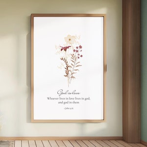 Peut inclure: Une impression encadrée avec une illustration aquarelle d'un bouquet de fleurs dans des tons de brun et de blanc avec quelques fleurs rouges. L'impression présente le texte "Dieu est amour" et un verset biblique de 1 Jean 4:16, "Quiconque demeure dans l'amour demeure en Dieu, et Dieu demeure en lui."