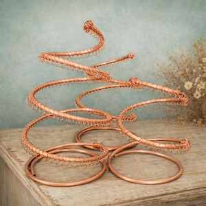 May include: A decorative sculpture crafted from copper-colored wire, featuring two circular bases that transition into an ascending, spiraling structure. The design incorporates a continuous coil of thin wire wrapped around a thicker wire frame.