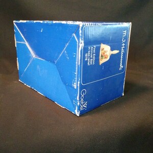 May include: A blue box with white text that reads "First Edition Annual Bell in bas-relief 1978" and "M.J. Hummel". The box is for a Goebel porcelain bell.