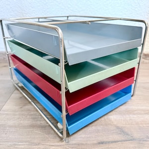 Puede incluir: Un organizador de escritorio de metal multicolor con cinco bandejas. Las bandejas son en tonos de azul, rojo, verde y gris, sujetas dentro de un marco de alambre cromado. El organizador está diseñado para uso en oficina o en casa.