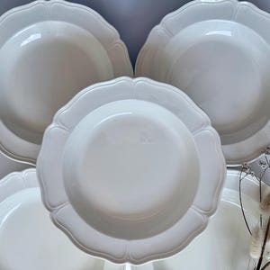 May include: A set of white ceramic plates with a decorative, scalloped edge. The plates are stacked, highlighting their elegant shape and glossy finish. The tableware is suitable for serving meals.