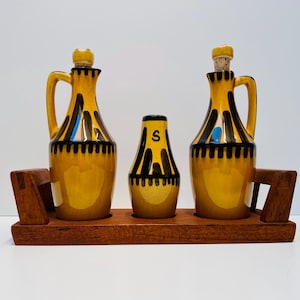 May include: A set of three ceramic condiment bottles with a black and yellow geometric design. The bottles are on a wooden tray.
