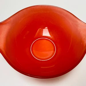 May include: A vibrant, red glass mixing bowl with a rounded shape and two handles. The bowl has a circular indentation in the center. This vintage kitchenware is perfect for mixing ingredients.