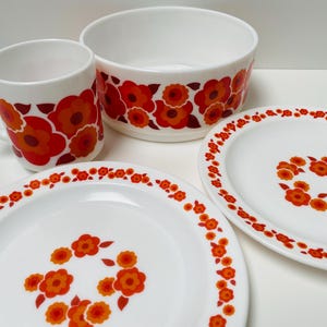 May include: A set of white ceramic dishes with a red and orange floral pattern. The set includes a bowl, a mug, and two plates.