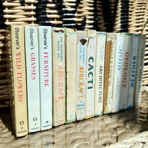 Könnte beinhalten: Eine Sammlung von Vintage-Observer's-Büchern mit Titeln wie "Wild Flowers", "Grasses" und "Aircraft". Die Buchrücken sind in verschiedenen Farben gehalten, mit Titeln in fetter Schrift. Die Bücher sind auf einer gewebten Oberfläche angeordnet.