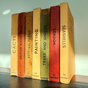May include: A collection of vintage books with titles including "Cacti," "British Birds' Eggs," and "Seashells." The spines are in various colors, with text in a serif font. The books are arranged vertically on a shelf.