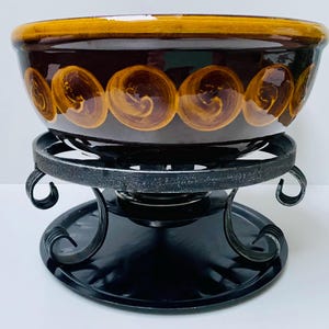 Può includere: Un pentolino per fondue in ceramica marrone con un motivo a spirale decorativo e un supporto in metallo nero con una base rotonda.