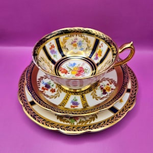 Peut inclure: Un ensemble de tasse à thé et soucoupe vintage avec un fond blanc et une bordure dorée et bleue. La tasse à thé et la soucoupe sont décorées de motifs floraux.