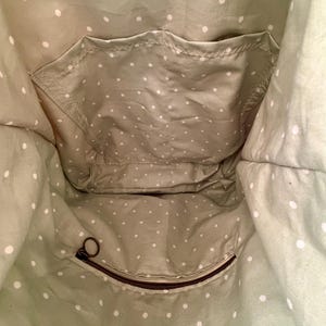 Puede incluir: El interior de un bolso de tela verde salvia con un patr&oacute;n de lunares blancos. Incluye un bolsillo abierto, un bolsillo con cremallera con un tirador marr&oacute;n y una etiqueta de tela blanca rectangular que dice Maple Moon Designs.