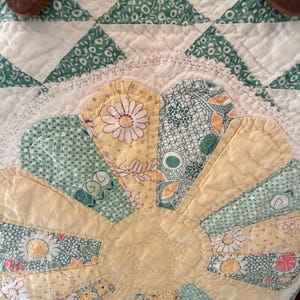 Puede incluir: Un bolso de tela acolchada con un dise&ntilde;o de flor grande aplicada con p&eacute;talos de patrones florales amarillos y verdes. El bolso tiene correas de cuero marr&oacute;n sujetas con remaches de metal color lat&oacute;n y un borde de encaje blanco alrededor.