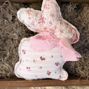 May include: A handmade fabric bunny with a floral pattern in pink and white. The bunny has a pink ribbon bow and is displayed in a wooden tray with dried moss. A charming Easter decoration.