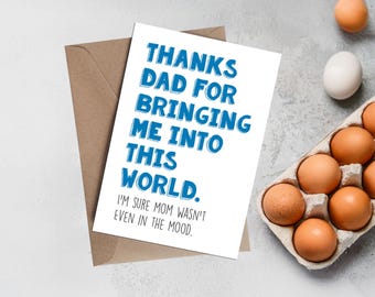 May include: A white greeting card with blue text that reads "THANKS DAD FOR BRINGING ME INTO THIS WORLD. I'M SURE MOM WASN'T EVEN IN THE MOOD." is placed on a brown envelope. Eggs are in a carton and scattered on a light gray surface.