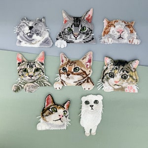 May include: Set of 8 iron-on patches featuring different cat designs. The patches are embroidered with colourful details and include a variety of cat breeds, including tabby, calico, and tuxedo cats.