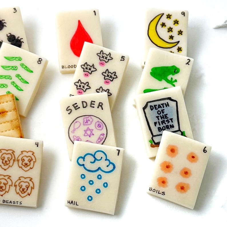 May include: A collection of small, rectangular cards with various illustrations and text. The cards feature images like a red drop, a frog, a crescent moon, and a tombstone. Some cards have numbers and words like "BLOOD" and "HAIL".