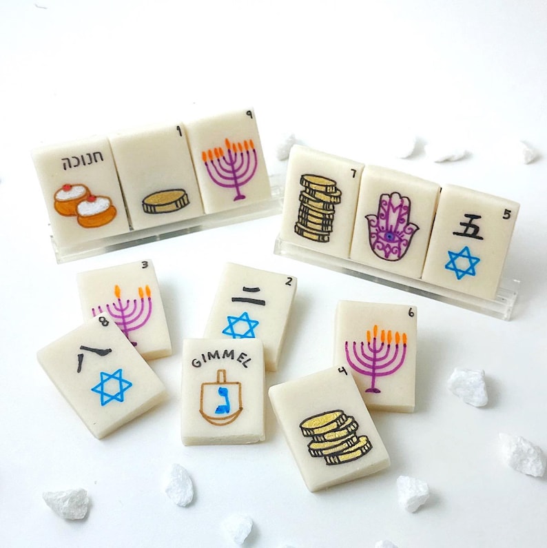 Op de afbeelding: Ivoor kleurige tegels met diverse illustraties en Hebreeuwse tekst. De tegels tonen afbeeldingen van een menora, munten, een Davidster en een dreidel. Sommige tegels hebben nummers en symbolen.