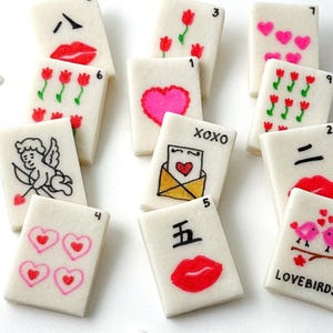 May include: A collection of white rectangular tiles with various hand-drawn designs. The designs include red lips, hearts, flowers, an angel, and the text "XOXO" and "LOVEBIRDS". Some tiles have numbers and Chinese characters.