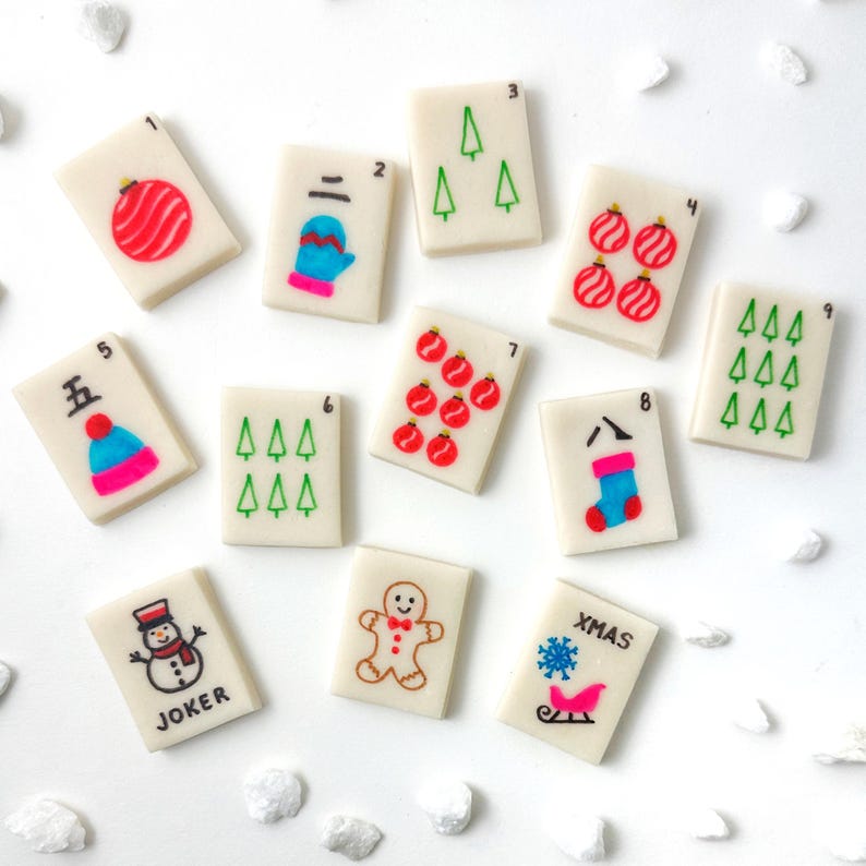 May include: A collection of Christmas-themed Mahjong tiles. Each tile features a number and a festive illustration, including ornaments, a mitten, Christmas trees, a stocking, a snowman, a gingerbread man, and a sleigh with the word "XMAS".
