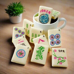 May include: A set of white mahjong tiles with colorful designs and numbers. The tiles include a joker tile, a dragon tile, and tiles with numbers 1 through 8. The tiles are arranged on a wooden surface.