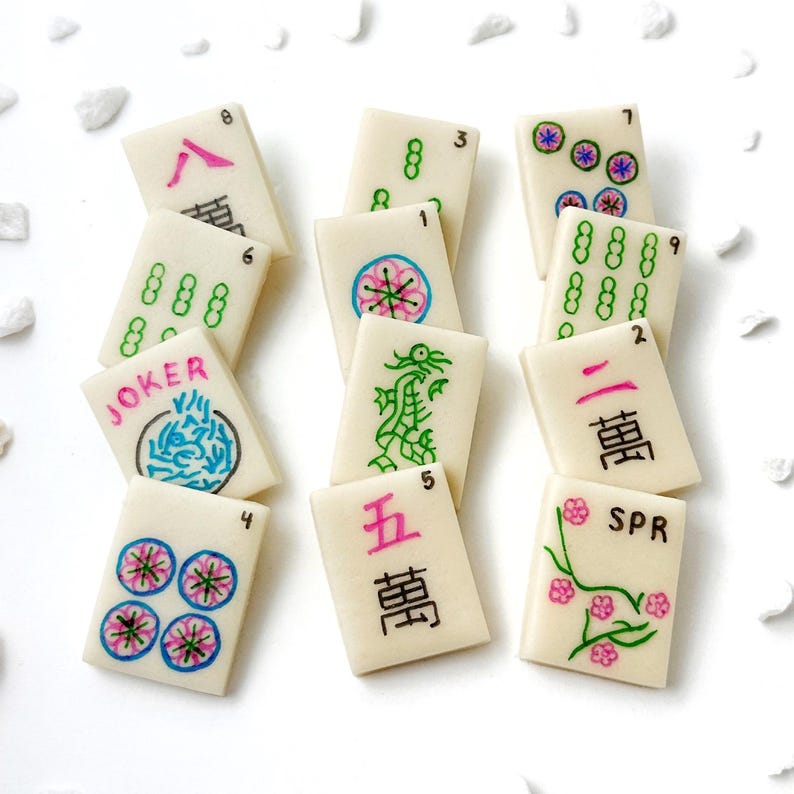 May include: A set of 11 mahjong tiles with various numbers, symbols, and characters. The tiles are white with black, green, pink, and blue markings. The tiles include numbers 1 through 9, the characters "JOKER", "SPR", and "萬" (meaning "ten thousand").